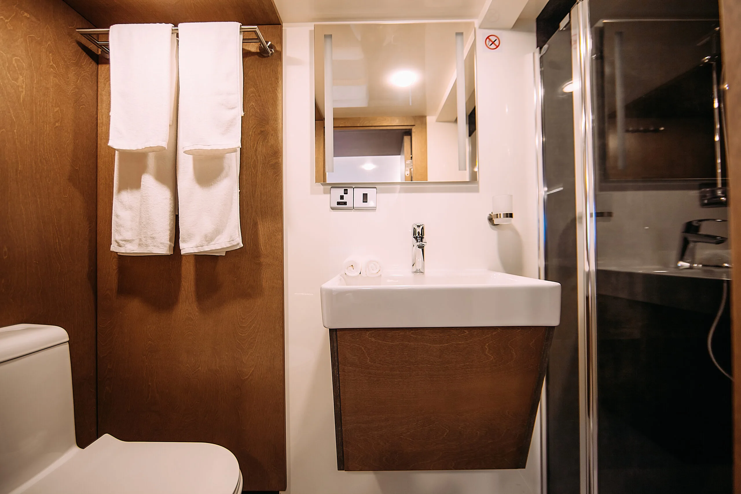 Book a private yacht in the Maldives Guest bathroom on Alice yacht with modern fixtures, towels and wood accents
