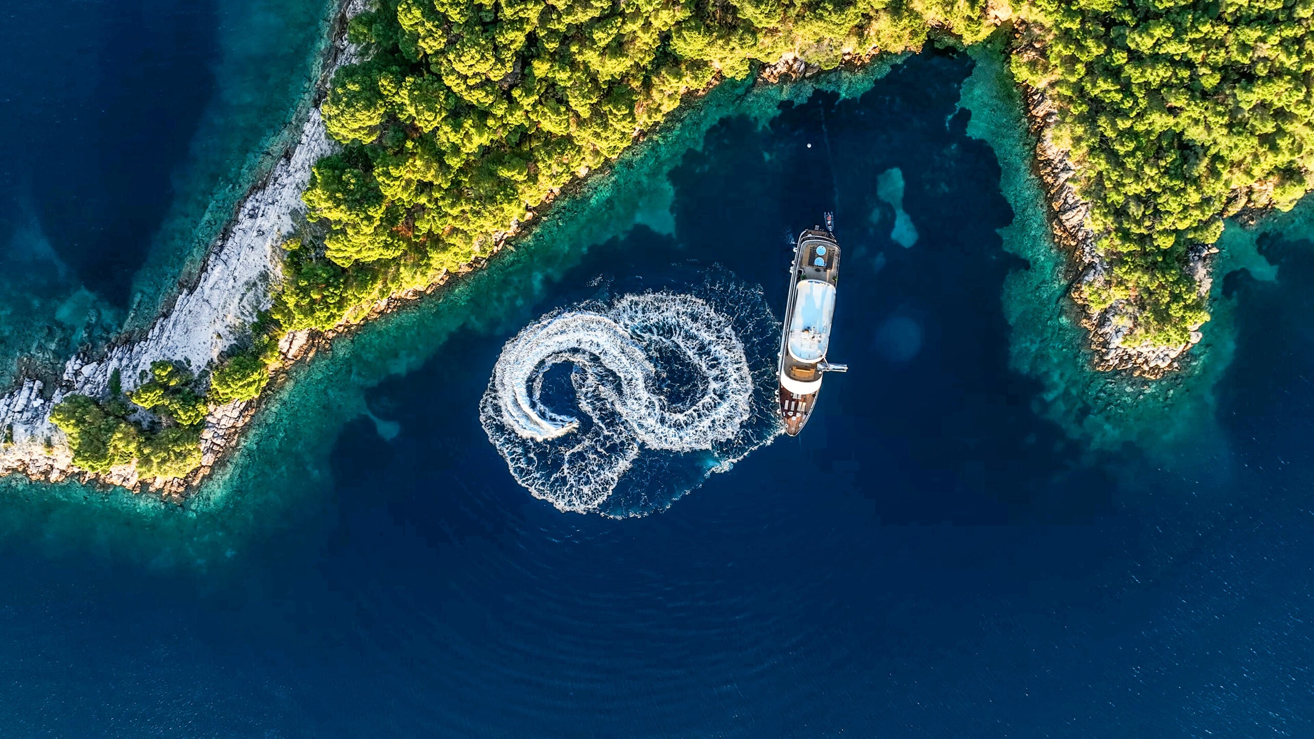 Aerial view of ARETHA luxury yacht making a figure-eight turn between two green Croatian islands.